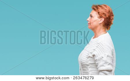 Atrractive senior caucasian redhead woman wearing winter sweater over isolated background looking to side, relax profile pose with natural face with confident smile.