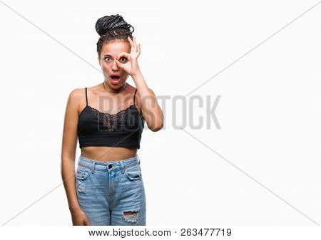 Young braided hair african american with pigmentation blemish birth mark over isolated background doing ok gesture shocked with surprised face, eye looking through fingers. Unbelieving expression.