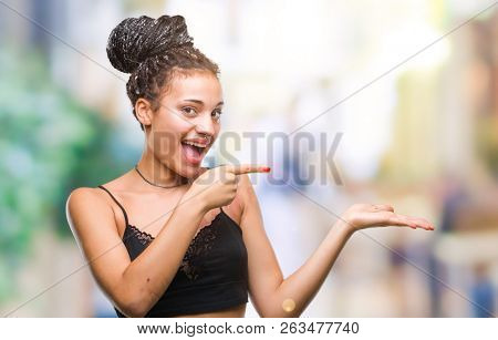 Young braided hair african american with pigmentation blemish birth mark over isolated background amazed and smiling to the camera while presenting with hand and pointing with finger.