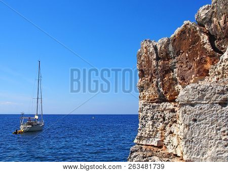 A Yacht On A Bright Calm Mediterranean Sea Next To Beautiful Rugged Cliffs On The Minorcan Coastline