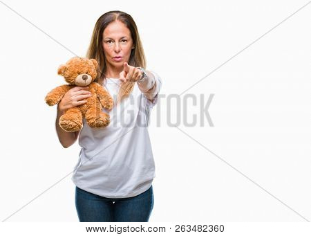 Middle age hispanic woman holding cute teddy bear plush over isolated background pointing with finger to the camera and to you, hand sign, positive and confident gesture from the front