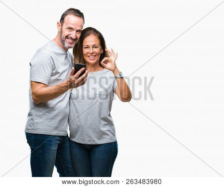 Middle age hispanic couple texting message on smartphone ver isolated background doing ok sign with fingers, excellent symbol