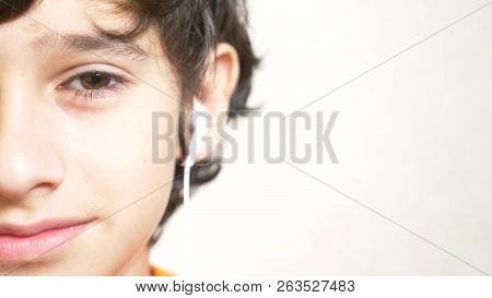 The Teenager Puts On White Headphones And Listens To Music. Close-up Of Half A Face. Copy Space.