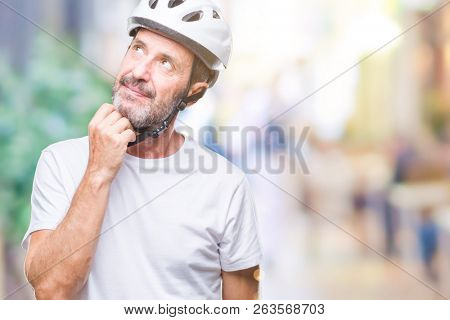 Middle age senior hoary cyclist man wearing bike safety helment isolated background with hand on chin thinking about question, pensive expression. Smiling with thoughtful face. Doubt concept.