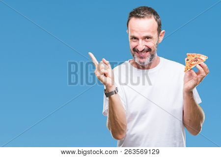 Middle age hoary senior man eating pizza slice over isolated background very happy pointing with hand and finger to the side