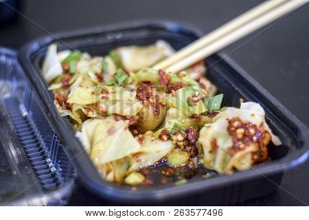 Closeup Of Chopsticks Holding A Chinese Wonton Dumplin Over A Takeout Container