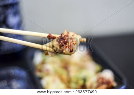 Closeup Of Chopsticks Holding A Chinese Wonton Dumplin Over A Takeout Container