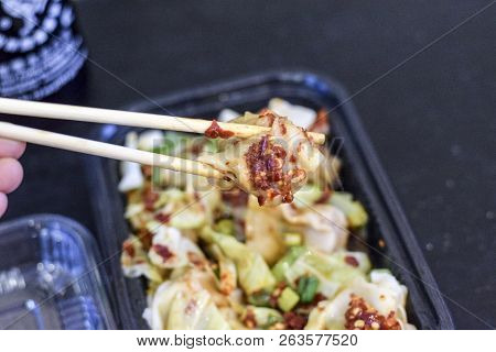Closeup Of Chopsticks Holding A Chinese Wonton Dumplin Over A Takeout Container