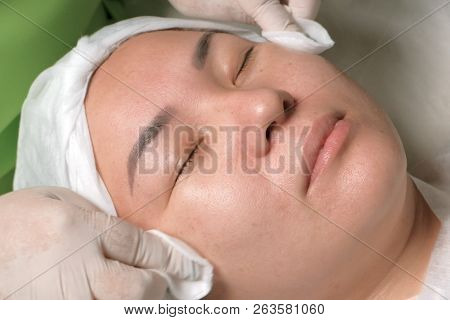 The Hands Of A Professional Beautician In White Gloves Wipe The Face Of A Relaxed Muslim Woman With 