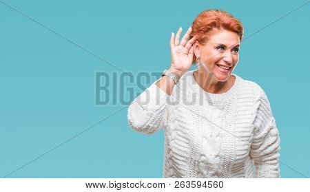 Atrractive senior caucasian redhead woman wearing winter sweater over isolated background smiling with hand over ear listening an hearing to rumor or gossip. Deafness concept.