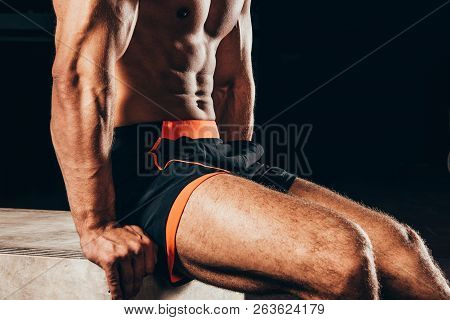 Cropped Shot Of Shirtless Athletic Man Sitting On Cube Isolated On Black