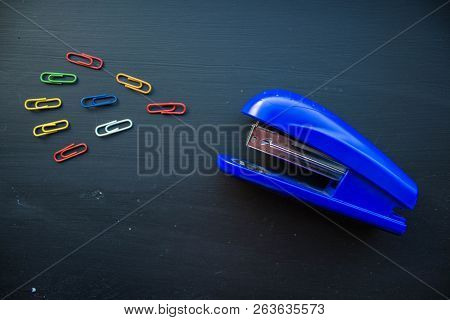 A Stepler And Colored Clips On Black Background