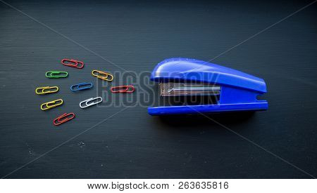 A Stepler And Colored Clips On Black Background