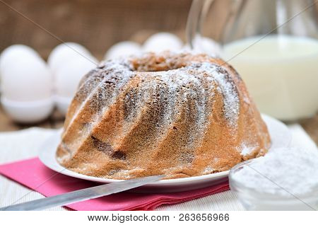 Homemade Bundt Cake Sprinkled With Sugar, Milk And Eggs In Background