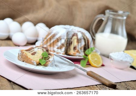Cut Of Bundt Cake Sprinkled With Sugar, Lemon, Melissa, Milk, Eggs And Butter