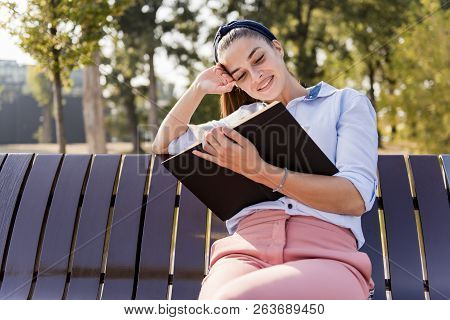 Beautiful  Young Woman  Holding  Open Book And Reading On Bench In Autumn Park