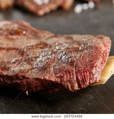 Hot Grilled Whole Flank Steak on Black Stone Background. Fresh Juicy Medium Rare Beef Grillsteak. Barbecue Meat Close Up