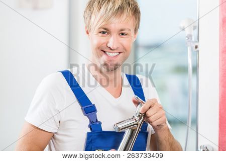 Close-up portrait of a cheerful maintenance worker looking at camera while holding a high-quality bathroom faucet in a modern sanitary ware shop