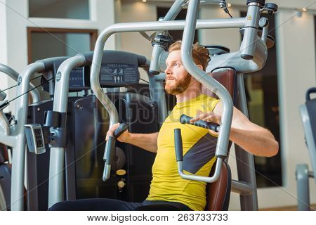 Portrait of a handsome bodybuilder smiling and looking at camera while exercising at a modern fitness machine for pectoral fly and deltoid workout
