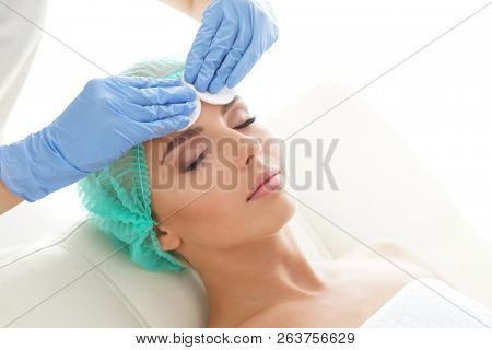 Cosmetologist cleaning face of a young woman with a cotton pads. Removing cosmetics with hygienic discs.
