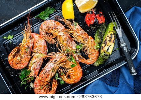 Traditional fried black tiger prawn with vegetable and lemon as top view in a black skillet 