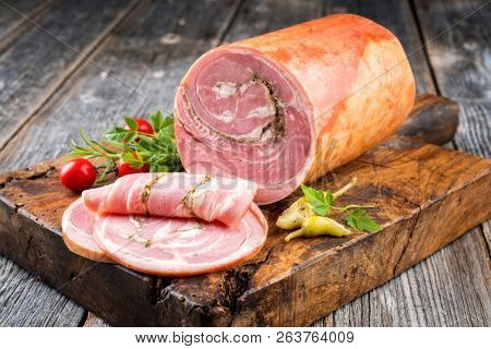 Traditional Allgauer veal roast roll sausage sliced and as piece with tomatoes and chili as closeup on an old rustic cutting board 