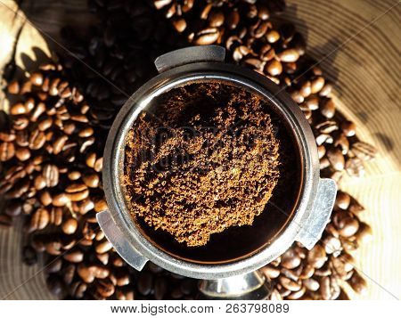 Close Up Of A Metal Portafilter Filled With Coffee Powder And Coffee Beans Around On Wooden Table