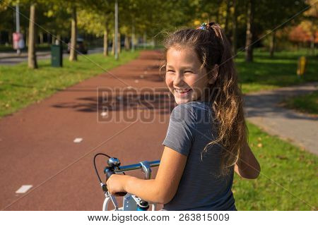Happy Child Rides A Bike On Bike Path. Cyclist Child Or Teenager Girl Enjoys Good Weather And Cyclin