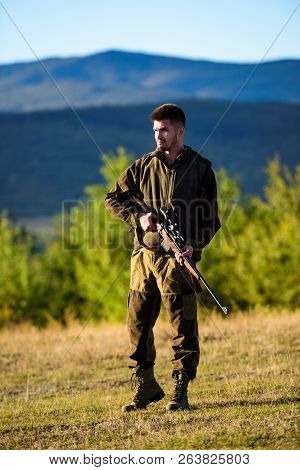Hunter Khaki Clothes Ready To Hunt Hold Gun Mountains Background. Hunter With Rifle Looking For Anim