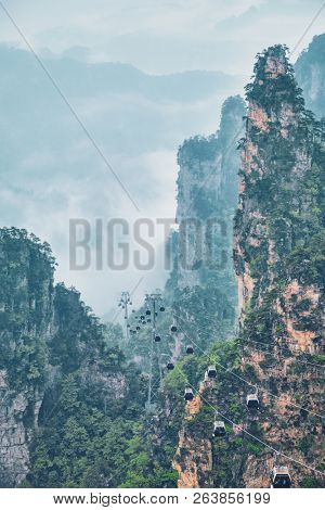 Famous tourist attraction of China - Zhangjiajie stone pillars cliff mountains in fog clouds with cable railway car lift at Wulingyuan, Hunan, China. With camera pan