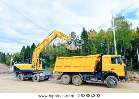 The Wheel Excavator Loads The Earth With A Bucket To The Body Of A Multi-ton Dump Truck On The Const