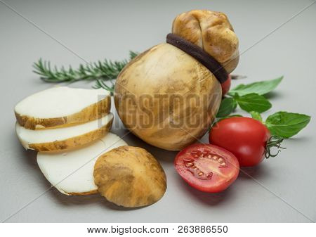 Traditional Italian smoked Scamorza cheese with herbs and tomatoes on gray background.