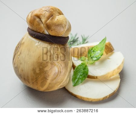 Traditional Italian smoked Scamorza cheese with herbs on gray background.