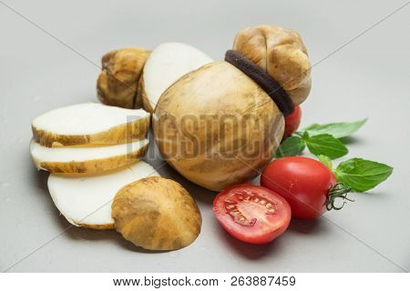 Traditional Italian smoked Scamorza cheese with herbs and tomatoes on gray background.