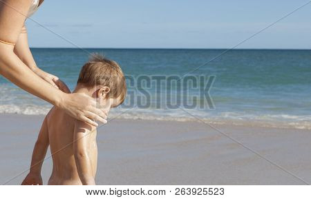Mother Applying Sunblock Cream To Her Little Son On Back. Idyllic Beach Background