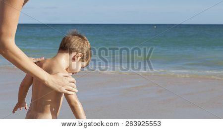 Mother Applying Sunblock Cream To Her Little Son On Back. Idyllic Beach Background