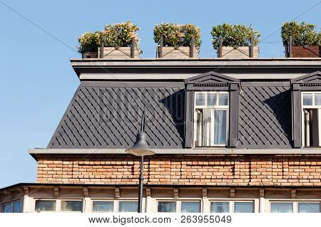 Attic Windows On The Building Roof With Flower Boxes At Sunny Day