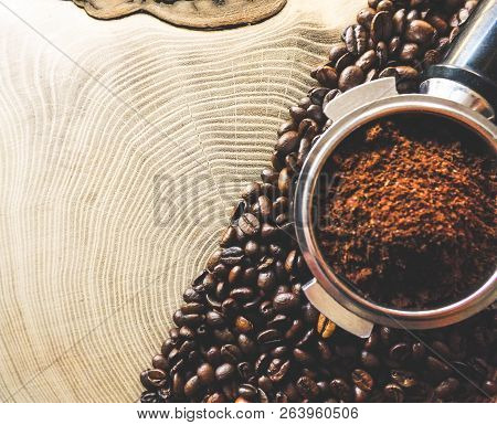 Close Up Of A Metal Portafilter Filled With Coffee Powder And Coffee Beans Around On Wooden Table