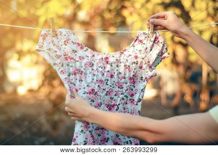 Flower Print T-shirt Hanging On A Clothespin Female Hand Nature On Blur Background