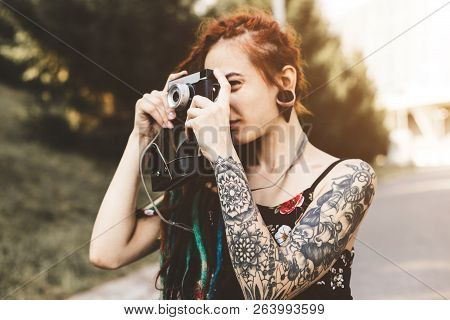 Young Girl With Tattoos And Dreadlocks Photographs Vintage Camera In The Park