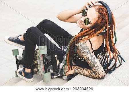 Young Girl With Tattoo And Dreadlocks Listening To Music While Sitting On The Steps