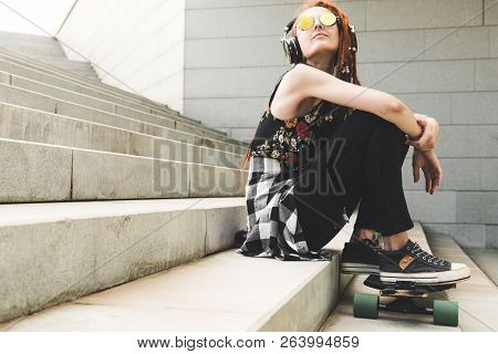 Young Girl With Tattoo And Dreadlocks Listening To Music While Sitting On The Steps