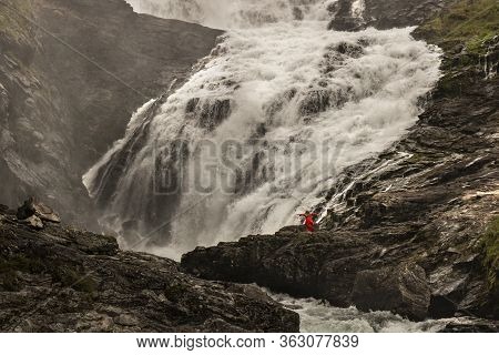 A Woman Wearing A Red Dress Dancing Next To Kjosfossen Waterfall In A Rocky Landscape In Norway