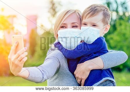 Attractive Mother Female Person And Little Boy Make Selfie On Phone In The Park On A Background Of G