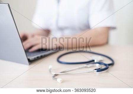 Unrecognizable Female Doctor In Uniform Uses A Laptop. Faceless Medical Worker Writes A Report On Th