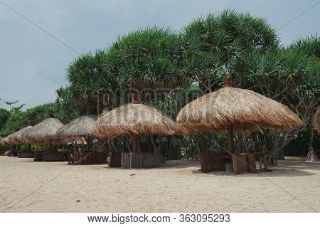 Beach Umbrellas From Straw On Tropical Sandy Beach. Sea Waves And Empty Sandy Beach At Sunset. Vacat