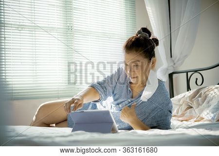 Woman With Protection Mask In Hand Lying On Sofa Bed In Home Living Room Chatting To Internet Device