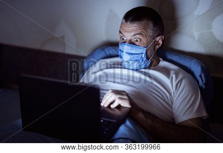 Covid-19 Anxiety. Scared Man Panicking Reading News On Laptop Lying In Bed At Home Overnight. Low Li
