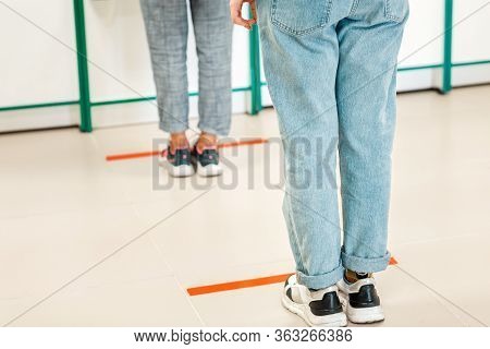 People Stand In Line, Legs Close-up. Attention Line On The Floor Of The Store To Maintain Social Dis