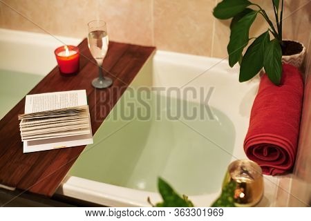 Bath With Flower Petals. Book, Candles And Glass Of Wine On A Wood Tray. Organic Spa Relaxation In C